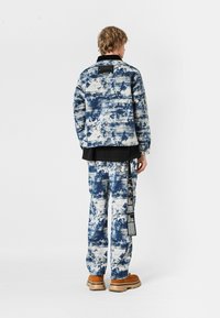 Chaqueta y pantalones de tela texturizada con un patrón azul y blanco, con un cuello negro y una etiqueta de acento en los pantalones. Calzado marrón.