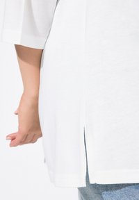 Weißes Baumwoll-T-Shirt mit kurzen Ärmeln, das über einen Seitenschlitz verfügt und lässig geschnitten ist, kombiniert mit hellen Jeans.