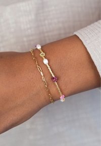 Goldene Kettenarmband mit Perlen und bunten Edelsteinen. Trägt man an einem Handgelenk mit glatter Hautstruktur.