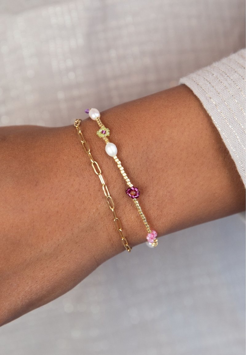 Goldene Kettenarmband mit Perlen und bunten Edelsteinen. Trägt man an einem Handgelenk mit glatter Hautstruktur.