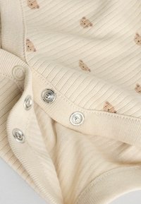 Țesătură din bumbac bej cu textură în relief; are model mic cu ursuleți maro; include capse metalice pe margine pentru închidere.