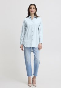 Camisa de botones azul clara con cuello, de mangas largas y corte relajado, combinada con jeans ajustados de lavado claro y tacones rosas claros.