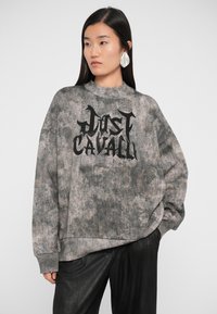 Sweatshirt cinza, oversized, com um design texturizado e uma grande impressão preta "Just Cavalli" na parte da frente. Apresenta um colarinho alto e um corte solto.