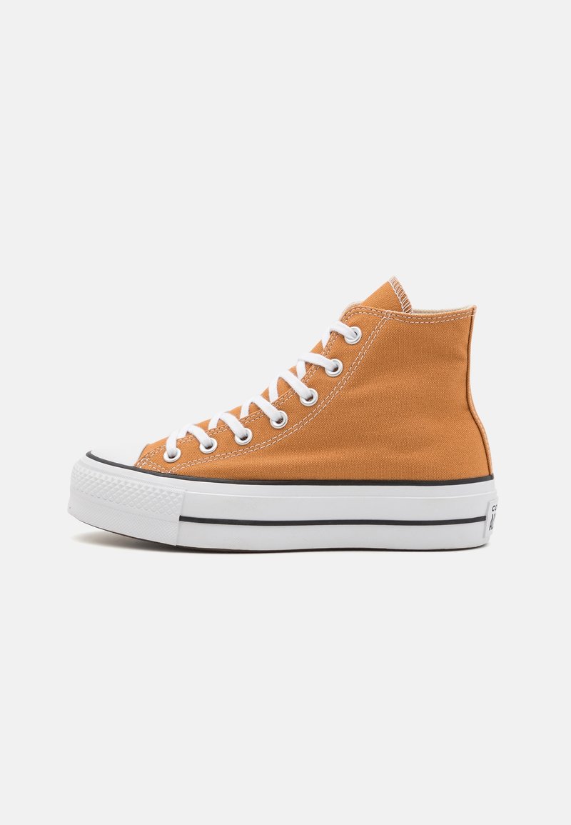Baskets montantes orange en toile avec semelle en caoutchouc blanche, lacets blancs et détail d'une bande noire sur fond blanc uni.
