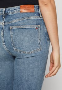 Jeans in denim azzurro chiaro con etichetta in pelle recante la scritta "TOMMY HILFIGER", design classico a cinque tasche e cuciture visibili.