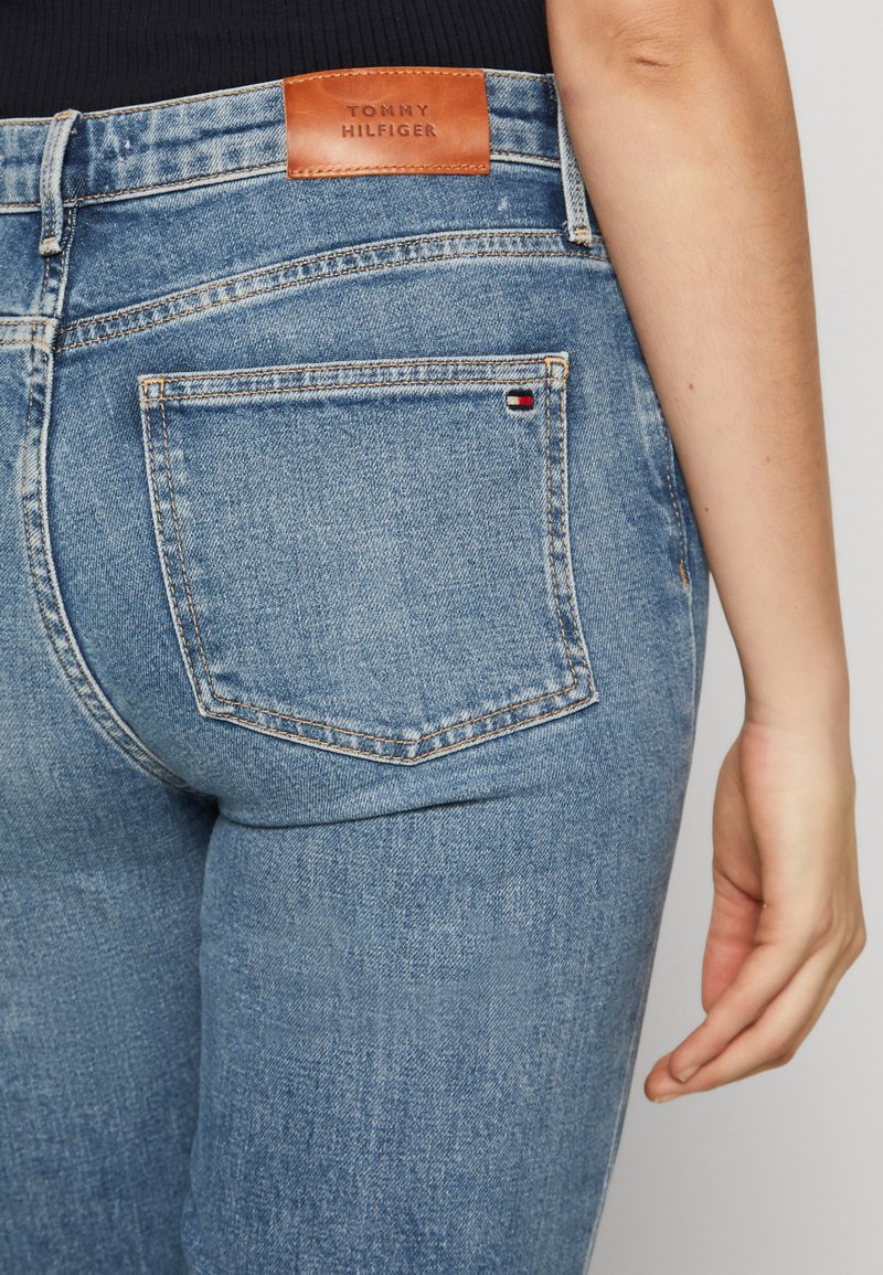 Jasnoniebieskie dżinsy z denimu z skórzaną metką z napisem "TOMMY HILFIGER", klasyczny pięciopocketowy fason oraz widoczne szwy.