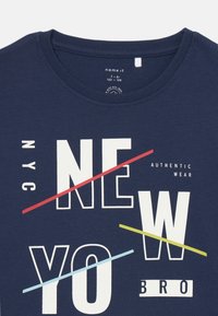 Námornícky modré bavlnené tričko s okrúhlym výstrihom. Grafický text v bielej, červenej, žltej a svetlomodrej farbe s nápisom "NEW YO NYC BRO AUTHENTIC WEAR."