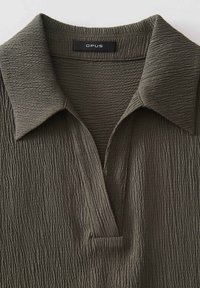 Dark olive green polo shirt with a textured, rippled fabric, featuring a classic collar and a short placket for a casual look.
