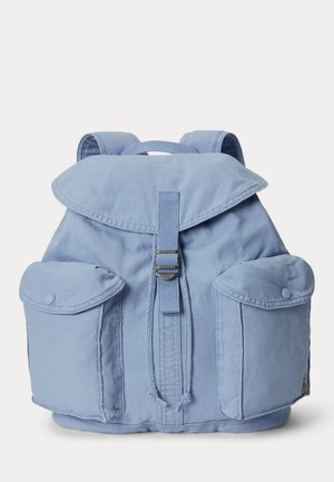 Zaino in tessuto azzurro chiaro con patta superiore, due tasche frontali con bottoni, spallacci regolabili e una cinghia centrale con fibbia in metallo.