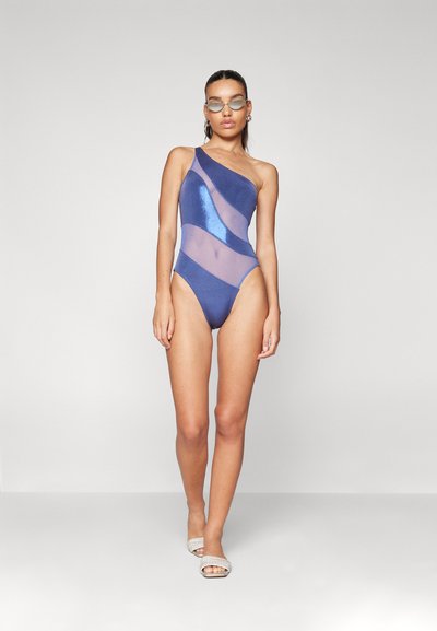 Maillot de bain une pièce bleu marine avec des panneaux transparents, un design asymétrique et des accents brillants. Texture lisse et ouvertures de jambes hautes.