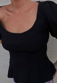 Musta muotoiltu toppi, jossa on neliön muotoinen pääntie ja pussimaiset lyhyet hihat. Sujuva kangas, jossa on pystysaumakirjontaa ja peplum-helma.