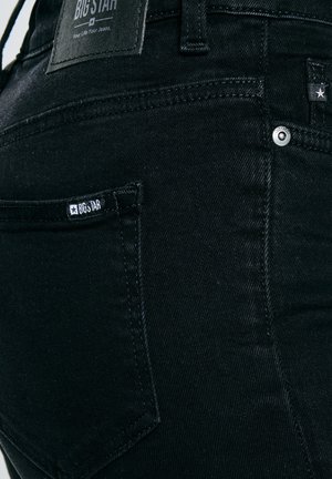 Zbliżenie na tylnią kieszeń czarnych jeansów z denimu z widoczną metką marki Big Star i metalowymi nitami.