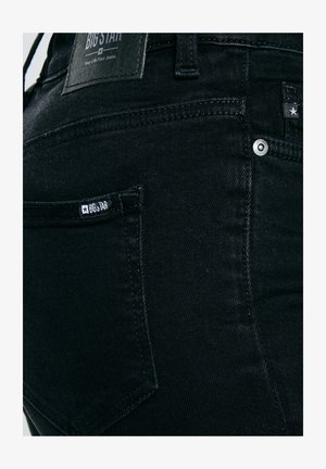 Close-up van de achterzak van zwarte spijkerbroek met zichtbare Big Star merklabel en metalen klinknageldetails.