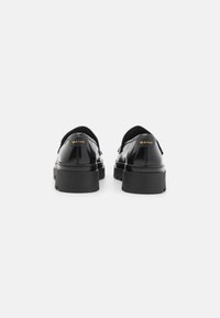 Schwarze Lacklederschuhe mit einer klobigen Sohle, abgerundeter Zehenform und dezentem goldenen Branding an der Ferse. Texturiertes, zum Hineinschlüpfen geeignetes Design.