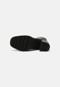Semelle de chaussure habillée noire avec grip texturé et petit talon carré, vue de dessous sur fond blanc.