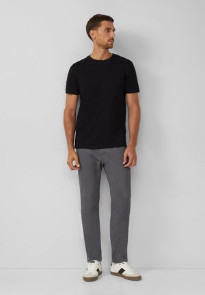 T-shirt noir à manches courtes, pantalon gris ajusté et sneakers blancs avec des accents noirs et bruns. Look simple et décontracté avec un design minimal.