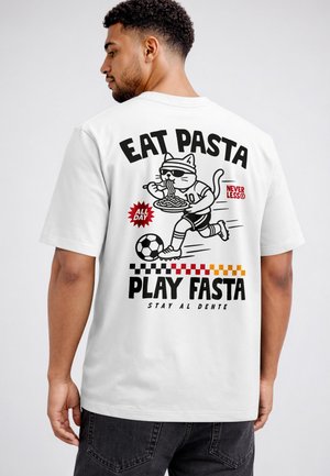 Man wearing white t-shirt with graphic of a cat playing soccer while eating pasta and text "Eat Pasta Play Fast Stay Al Dente."