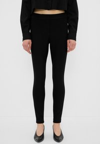 Leggings neri realizzati in tessuto elasticizzato, caratterizzati da un'alta vita e un design aderente che si restringe alle caviglie. Nessun motivo visibile.