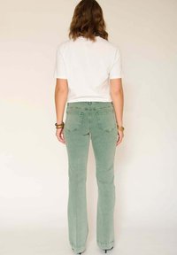 Jean évasé vert clair à taille haute, avec quatre poches et un tissu doux et texturé. Associé à un t-shirt blanc uni à manches courtes.