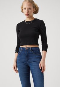 Musta ribbed pitkähihaine crop-top, joka on yhdistetty sinisiin korkeavyötäröisiin farkkuihin. Sisältää pienen etutaskun ja ruskean nappiyksityiskohdan.