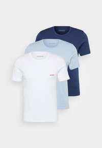 Three short-sleeve t-shirts in white, light blue, and navy, made from cotton, featuring a round neckline and small red logo on the white shirt.