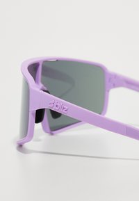 Lunettes de soleil en plastique violet avec des verres gris foncé, présentant un design géométrique robuste et le logo "bliz" sur la branche.