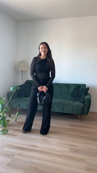 Μαύρη διαφανής μπλούζα με κομμάτια πουά και μακριά μανίκια συνδυασμένη με μαύρο φαρδύ παντελόνι. Κρατώντας μια μαύρη τσάντα υφής, με πράσινο καναπέ στο φόντο.