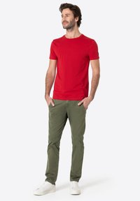 Rotes Baumwoll-T-Shirt mit Rundhalsausschnitt, kombiniert mit olivgrünen Chinos und weißen Sneakers. Das T-Shirt hat kurze Ärmel und eine figurbetonte Passform.