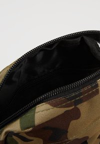 Pochette in tessuto a motivo camouflage con chiusura a zip nera. Interno foderato in materiale nero, con una consistenza morbida e cuciture rinforzate.