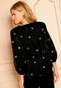 Top en velours noir avec des embellissements en argent en forme d'étoile, des manches bouffantes et une taille froncée, mettant en valeur une texture douce.