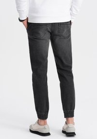 Pantalones de chándal negros con un corte ajustado y puños elásticos. Hechos de denim, presentan bolsillos traseros y una textura suave.