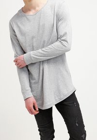 Grå långärmad t-shirt med rund halsringning och avslappnad passform, gjord av mjukt tyg. Matchas med svarta slitna jeans.