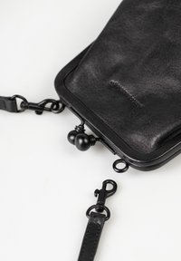 Schwarze Lederclutch mit Metall-Kiss-Lock-Verschluss, abnehmbar vom schwarzen Lederband mit Drehhaken, auf weißer Oberfläche.