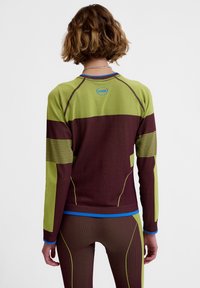 Langærmet atletisk top i grøn og bordeaux med ribstrikkede detaljer og blå kant. Designet inkluderer farveblokering og en tætsiddende silhuet.