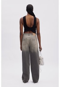 Top negro sin mangas con un diseño de espalda retorcida, combinado con jeans de pierna ancha en degradado gris que presentan un parche de logo y un bolso blanco texturizado.