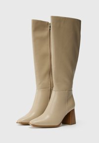 Beige Kunstlederkniehohe Stiefel mit spitzen Zehen, einem goldenen Reißverschluss an der Seite und einem gestapelten, strukturierten Holzabsatz.