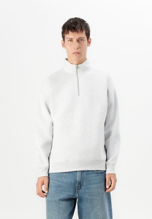Gray zip-up sweatshirt with a high collar, soft texture, and ribbed cuffs. Worn with light blue jeans. Simple and minimalistic design.