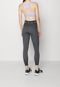 Purple sports bra with crisscross straps; gray textured leggings with vertical stripes; black athletic shoes with white soles.