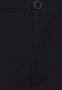 Pantaloni neri realizzati in un tessuto liscio, con chiusura frontale a bottone, una tasca singola e dettagli cuciti lungo le cuciture.