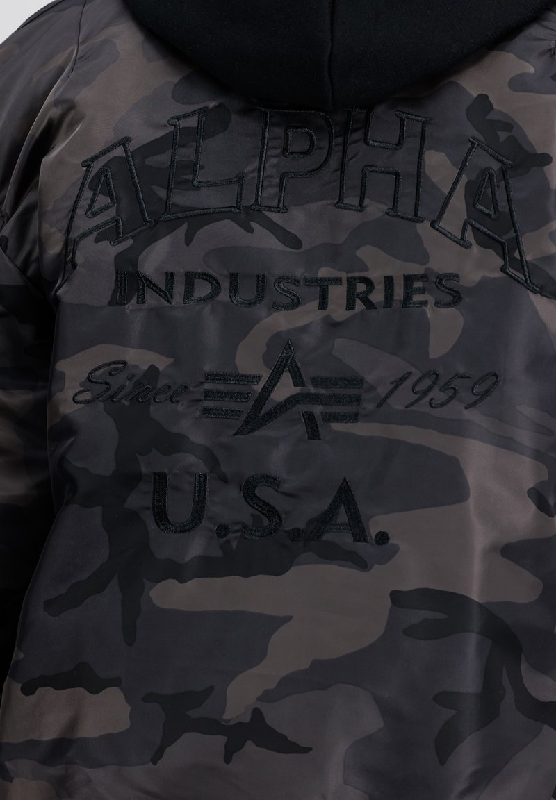 Giacca a motivo mimetico in nero e grigio con testo ricamato "ALPHA INDUSTRIES" e logo; tessuto liscio con cappuccio.