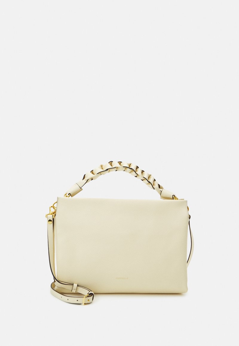 Ljusbeige läderhandväska med ett flätat handtag i toppen och en avtagbar axelrem. Har gulddetaljer och en slät yta.