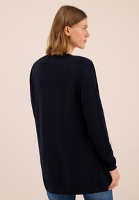 Langärmliger, dunkelblauer Pullover mit geradem Schnitt und rundem Halsausschnitt. Die glatte Textur und die seitlichen Schlitze am Saum erhöhen den Tragekomfort.