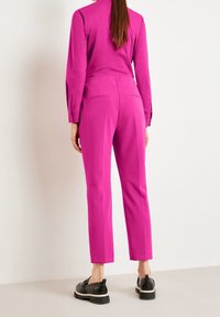 Pantaloni fucsia su misura con vestibilità slim, dotati di tasche posteriori e una texture di tessuto liscia. Abbinati a scarpe con tacco piatto nere.