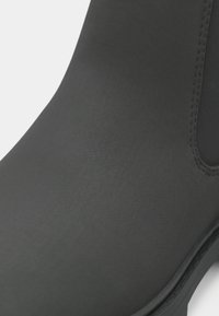 Botín negro impermeable hasta el tobillo con un acabado mate suave y paneles laterales elásticos. Diseño de punta redondeada y suela plana.