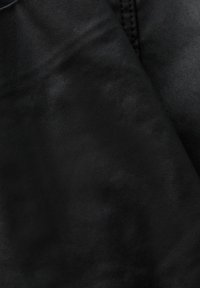 Gros plan sur un tissu noir avec des coutures visibles et de légères variations de texture dans le matériau.