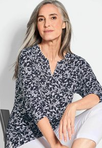 Zwart-wit bloempatron blouse met 3/4 mouwen en een V-hals. Zacht stof valt soepel, met geplooide accenten bij de mouwmanchetten.