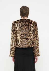 Persona con cabello corto castaño que lleva una chaqueta de piel sintética de leopardo y una falda negra larga, vista desde atrás contra un fondo blanco.