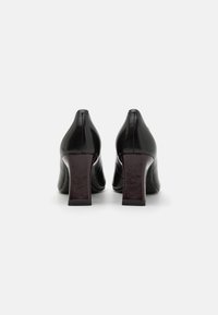 Chaussures à talons hauts noires avec une finition brillante, dotées d'un talon carré bordeaux texturé et d'un design à bout pointu.