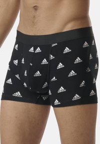 Boxer breif neri con loghi Adidas bianchi stampati in un motivo ripetuto. Presentano un cintura elastica e un design aderente.