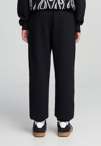 Pantaloni della tuta neri, taglio a cono, con vita elastica. Tessuto morbido, design semplice. Indossati con sneakers nere e bianche dotate di suola in gomma.